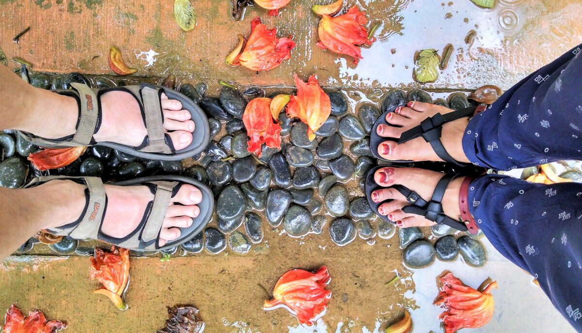 Looking down at two people's feet standing on wet rocks surrounded by colorful leaves
