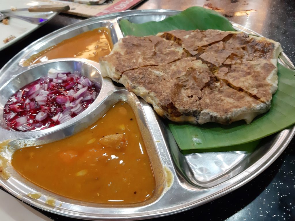 Plate of malaysian food with pancake, curry, and diced onions