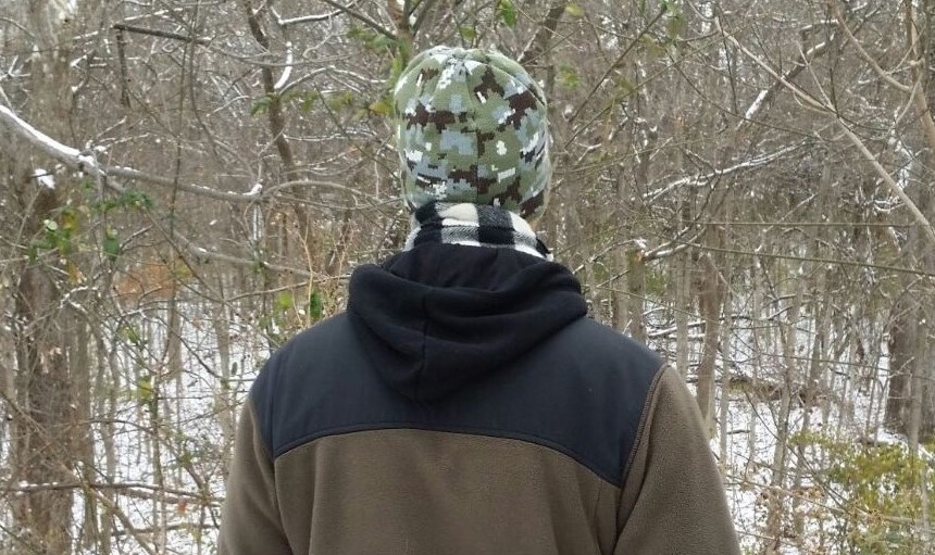 author shot from behind wearing hat and coat in the woods during winter