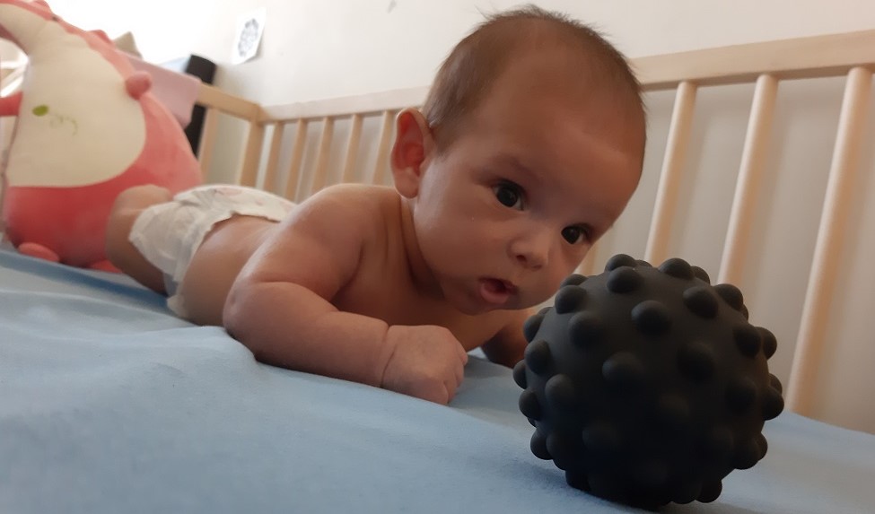 Baby boy on his stomach focusing on black toy ball in his crib
