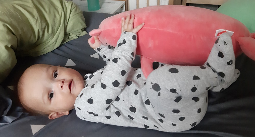 Baby boy in spotted onesie cuddling stuffed toy