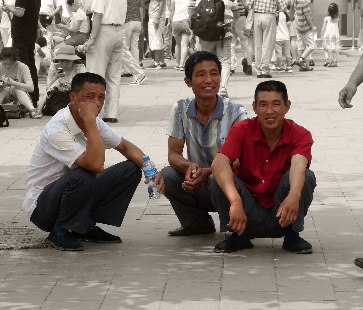 stock photo of three asian men squatting on a public sidewalk
