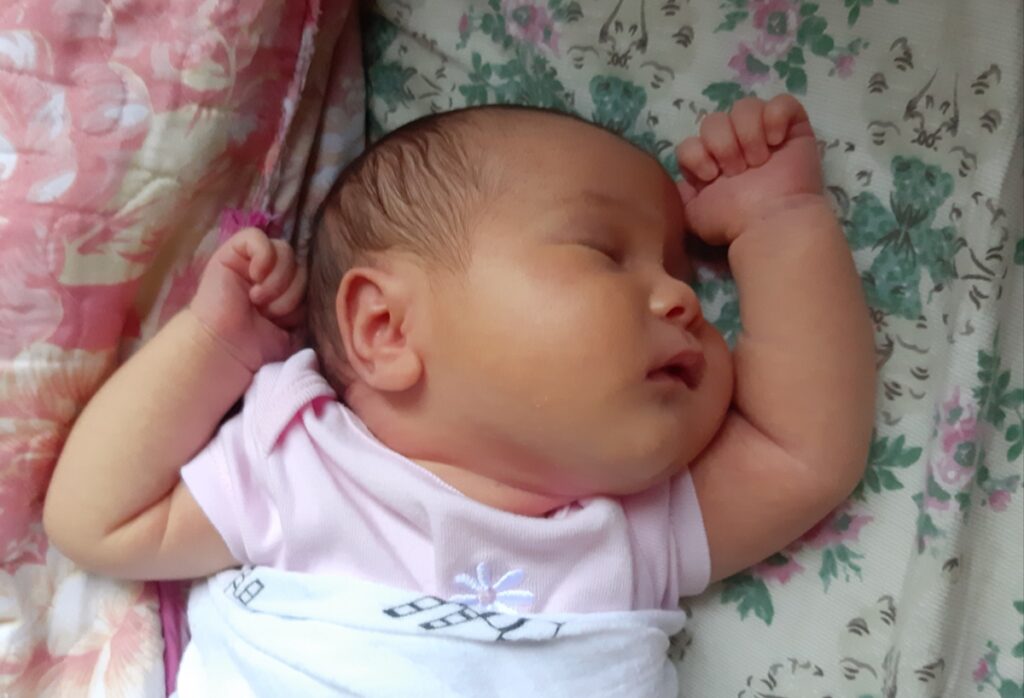 Baby girl sleeping with arms up and chubby cheeks