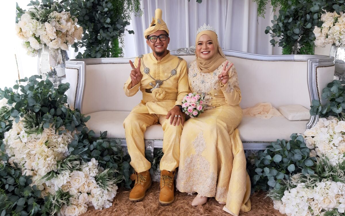 malaysian newlyweds wearing elaborate yellow wedding outfits surrounded by white flowers