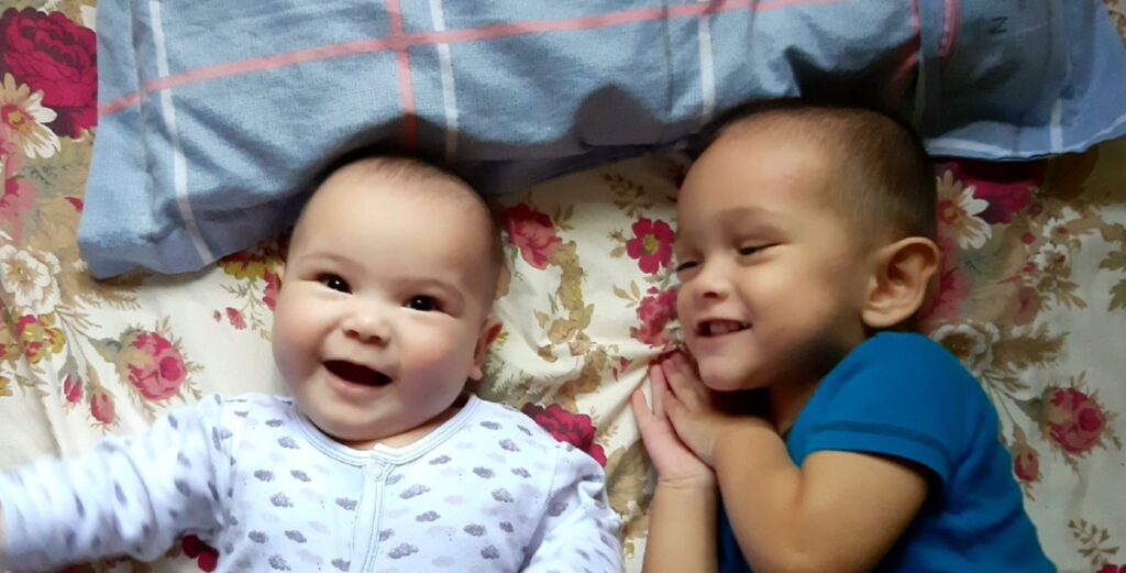 baby brother and sister laying next to each other in bed and both smiling