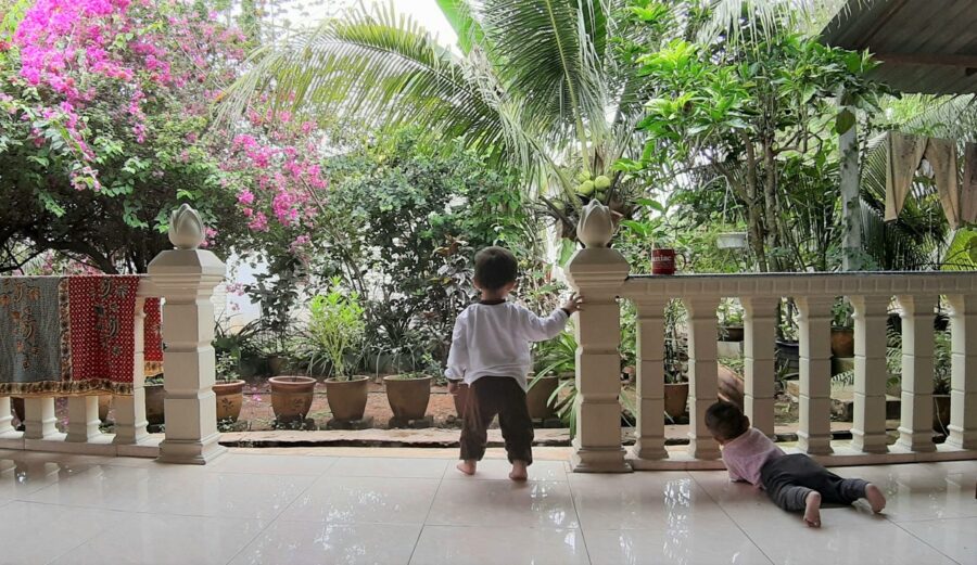tropical veranda with two toddlers staring at lush green garden