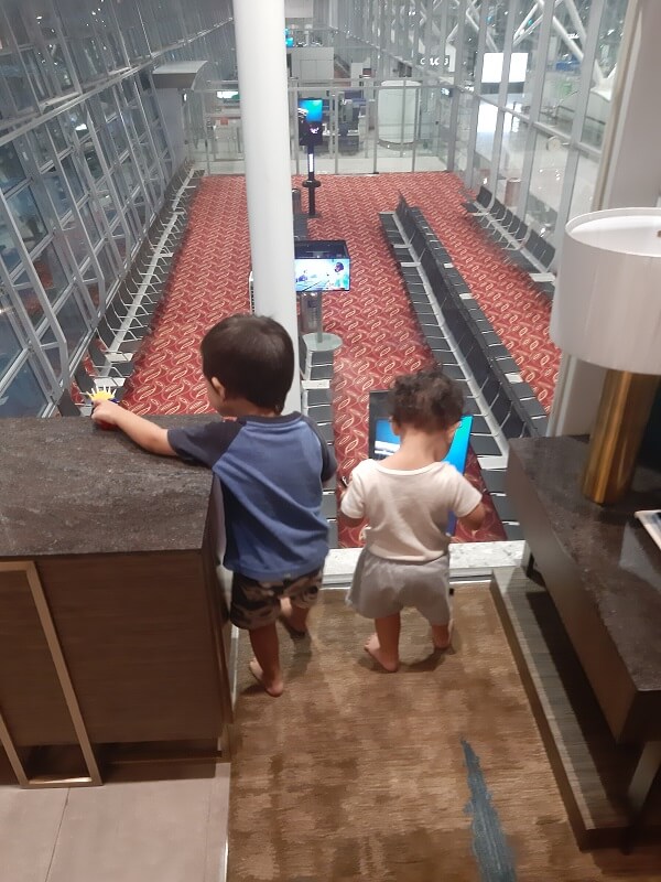Toddlers playing near window overlooking airport gate with rows of seats