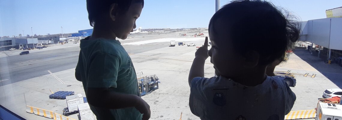 Toddlers at window looking out at sunny airport tarmac