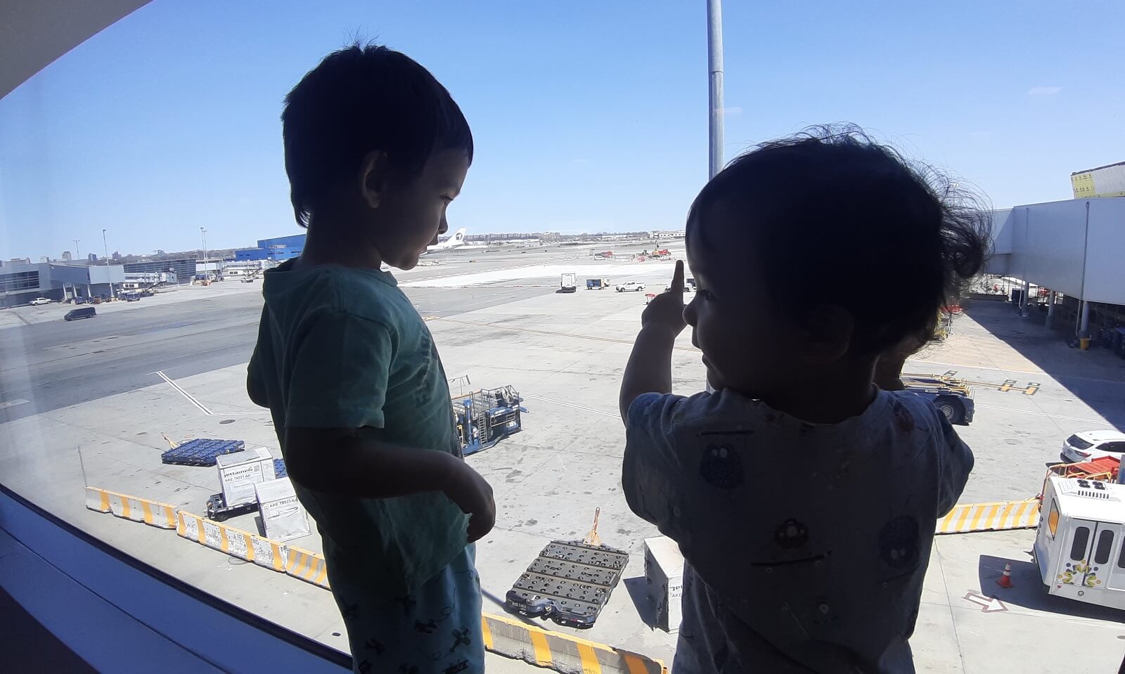Toddlers at window looking out at sunny airport tarmac