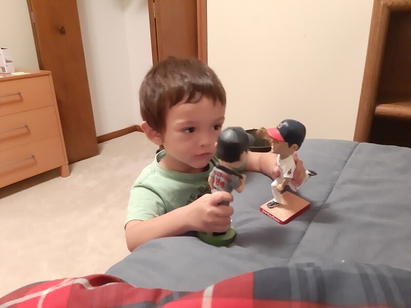 Toddler Adam playing with bobblehead toys on a bed