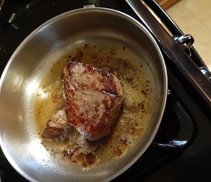Brown steak cooking in frying pan