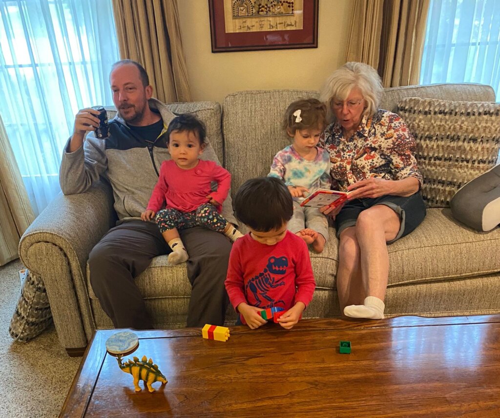 Family sitting together on couch, grandma reading to child