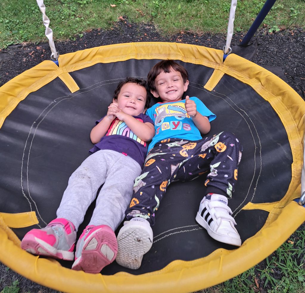 Two kids laying together smiling on a big playground swing