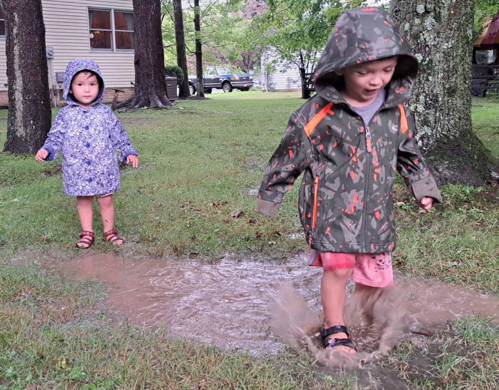 Kids wearing rain coats and splashing in a mud puddle