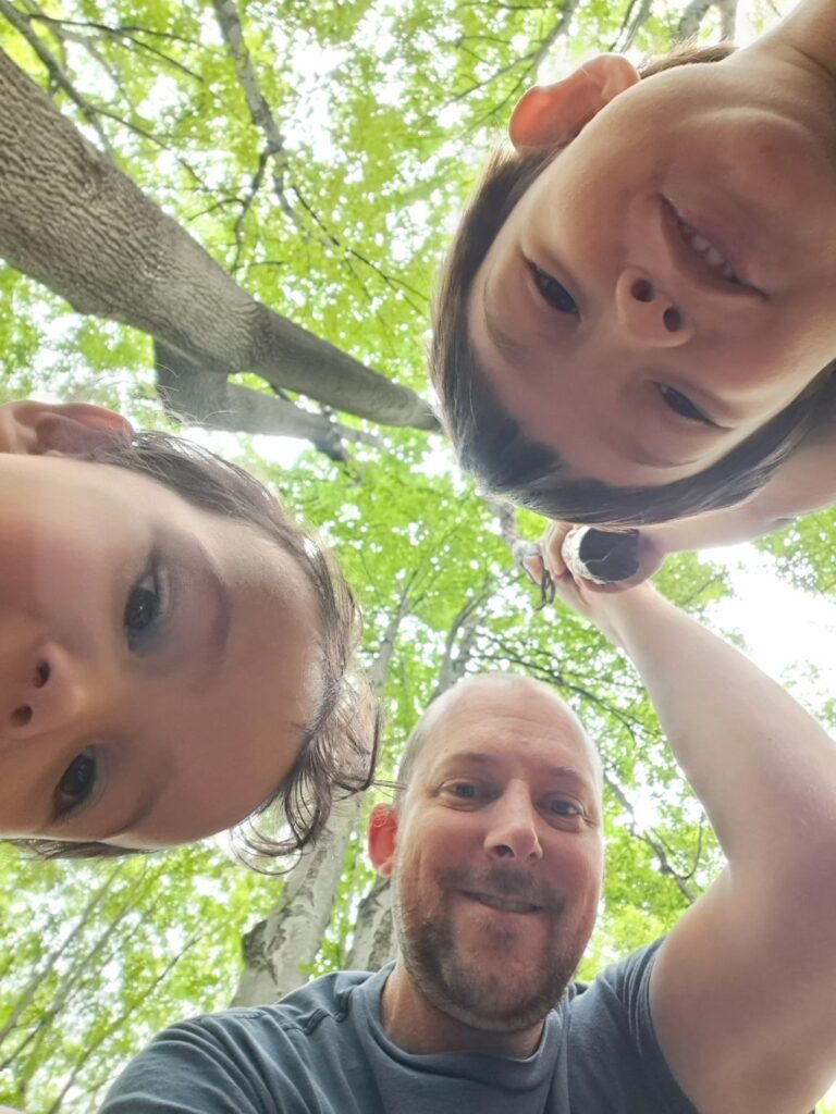 Father and kids looking down at the camera in a green forest