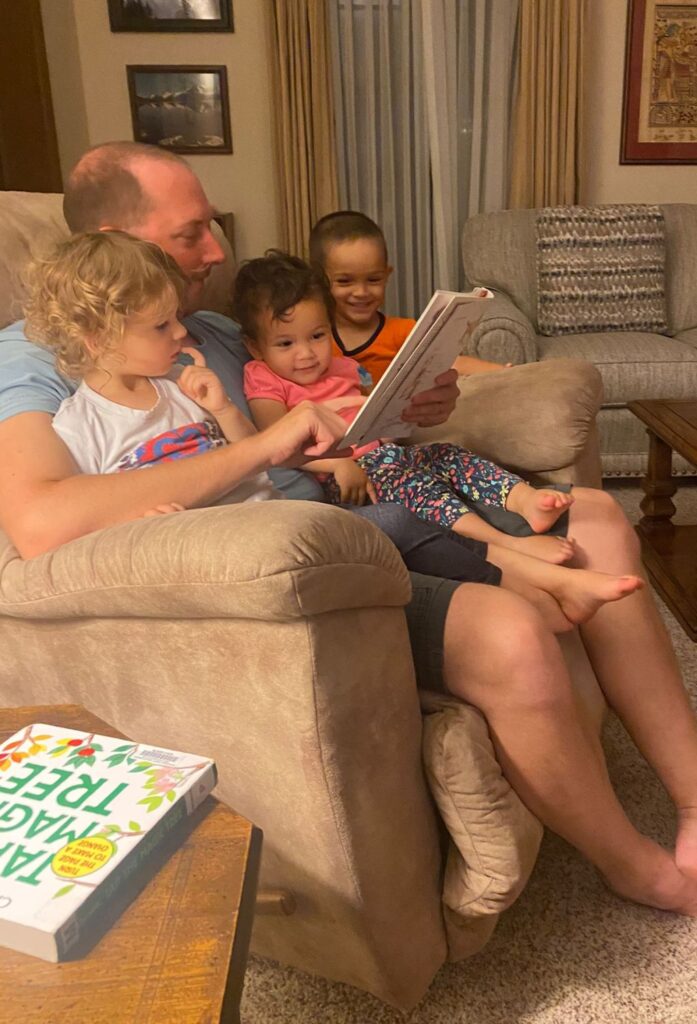 Author seated in recliner with three toddlers reading a story