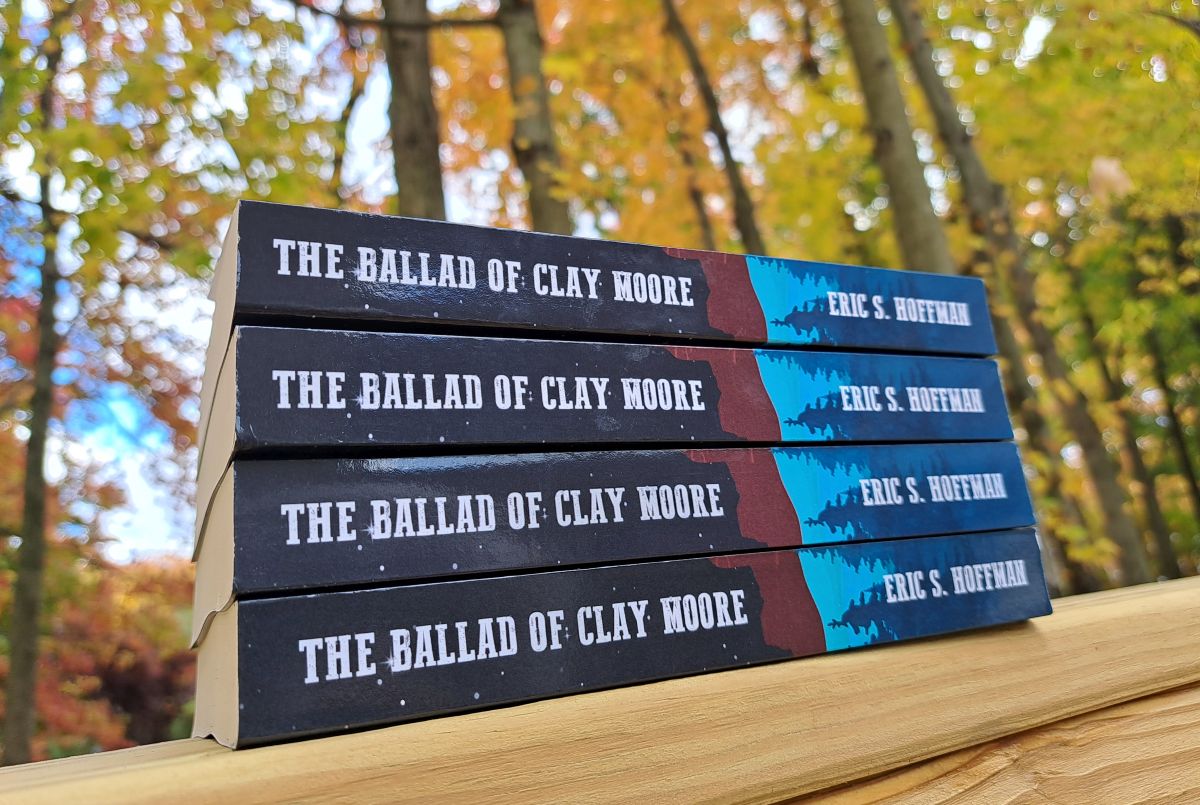 stack of paperback books on a wooden rail with colorful trees in the background