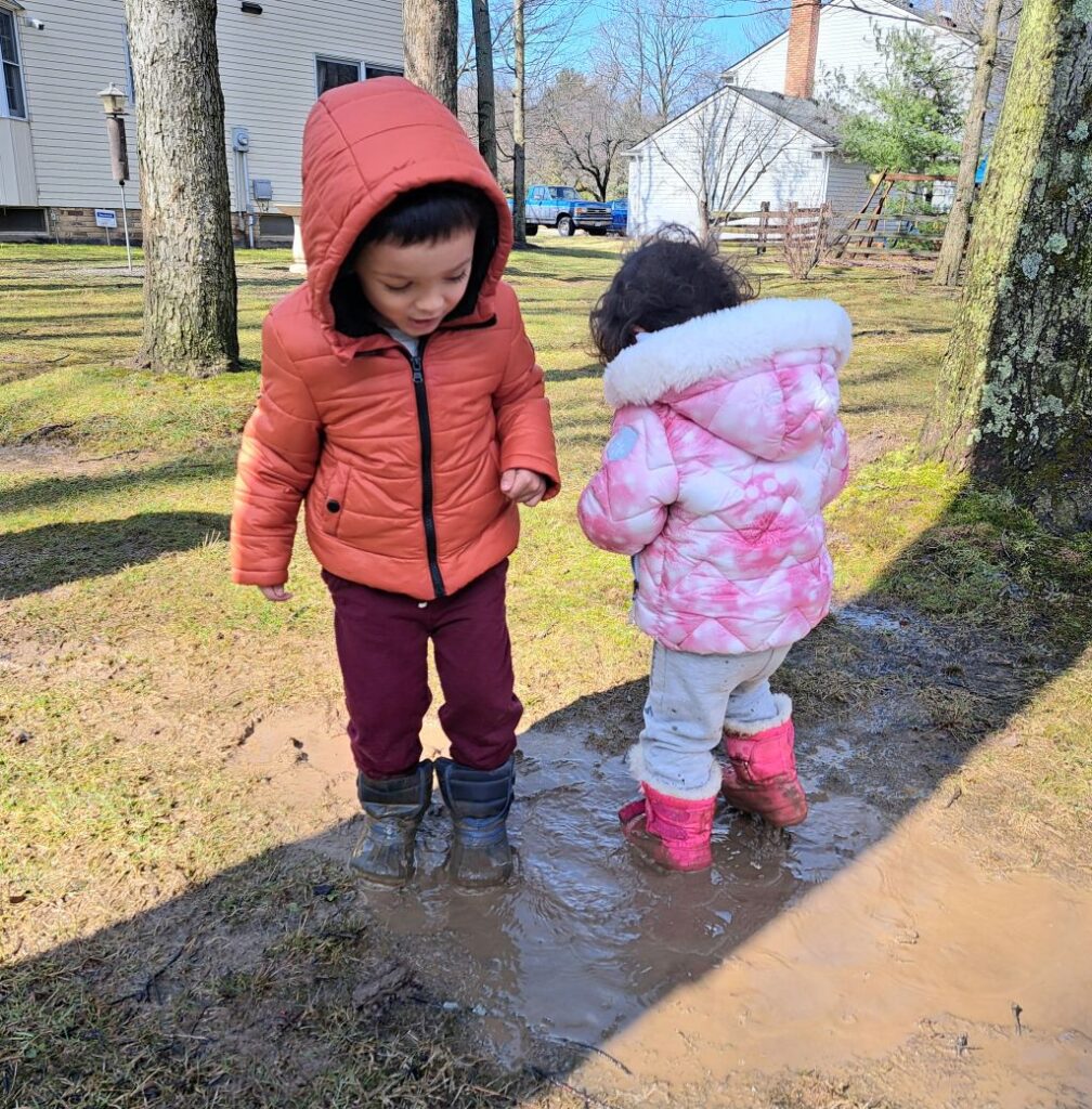 Kids in coats and boots standing in mud puddle