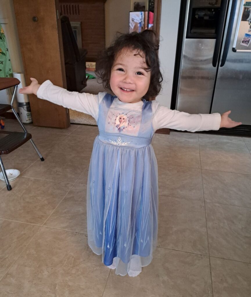leila standing with arms spread out smiling in a purple princess dress