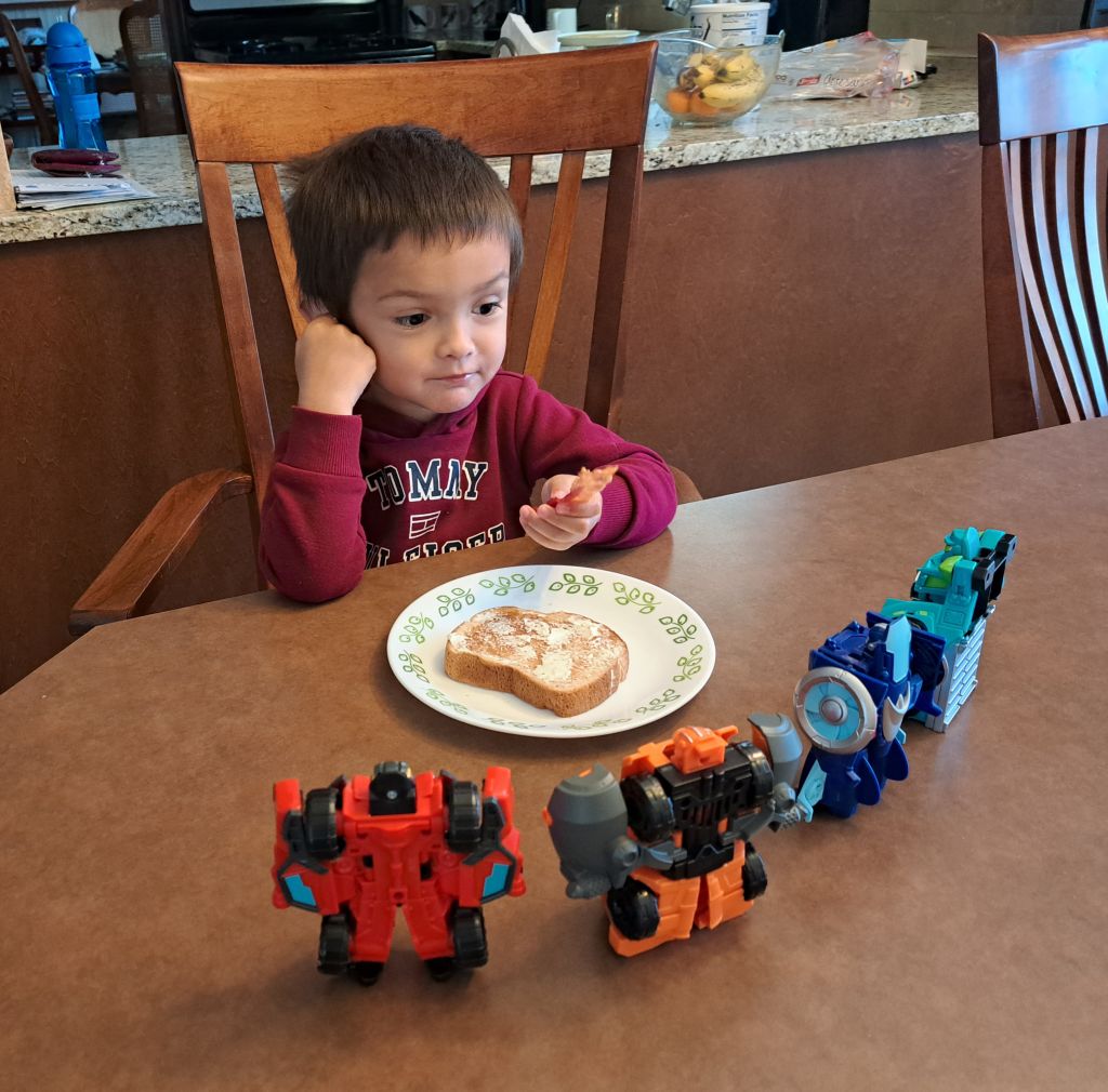 Adam eating toast with robot toys lined up on the table in front of him